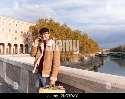 Smiling young Arab man talking on phone with shopping bags in hand Stock Photo