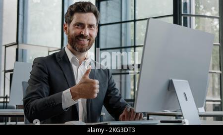 Middle-aged adult bearded 40s businessman worker working with computer in office showing thumb up. Manager man boss male company CEO typing working Stock Photo