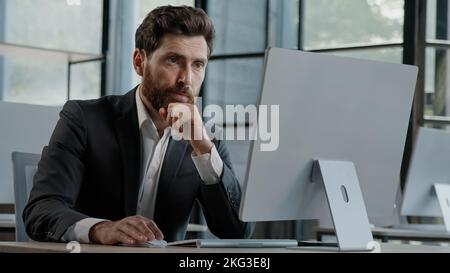 Busy pensive focused Caucasian bearded adult 40s man CEO company worker manager boss businessman working on computer in office searching solution of Stock Photo