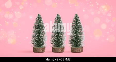Mini decorative Christmas trees against pink bokeh background. Stock Photo