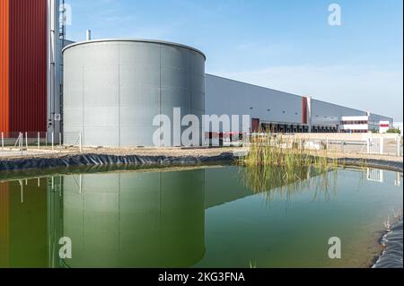Low angle perspective shot of round shaped water tank in front of warehouse building with reflection on water pool Stock Photo