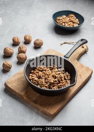 Roasted walnuts in black pan on cutting board and walnut shells against concrete background. Copy space. Stock Photo