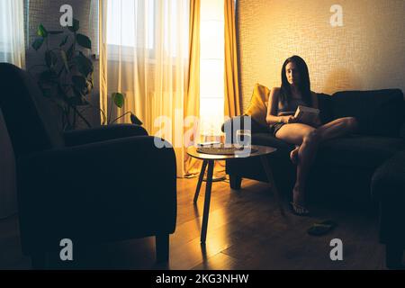 Close up thoughtful worried calm caucasian woman alone sit at home drink coffee with book in hands. Feeling lonely single woman with no man in 30s Stock Photo