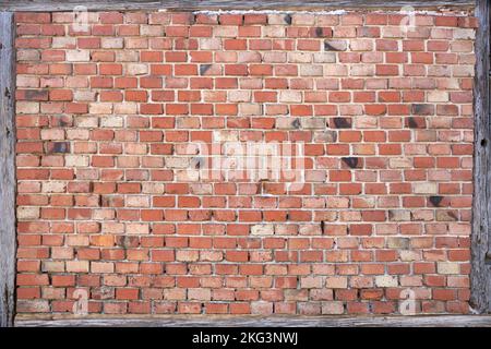 Old red brick wall framed by weathered wooden beams Stock Photo
