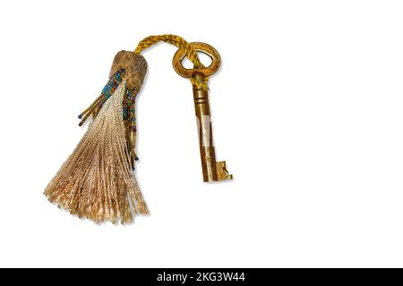 Old fashioned gold key hanging on a tassel, isolated on a white background. Clipping path. Stock Photo