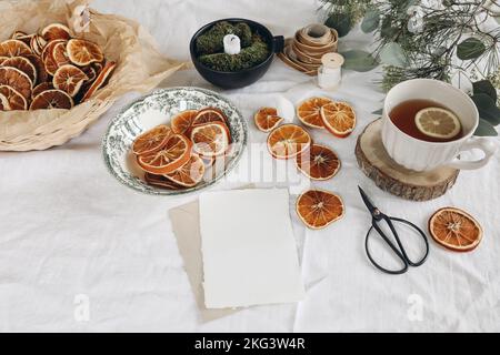 Traditional Christmas still life. Cup of tea, dry oranges and pine, eucalyptus tree branches on white linen table cloth. Blank greeting card mockup Stock Photo