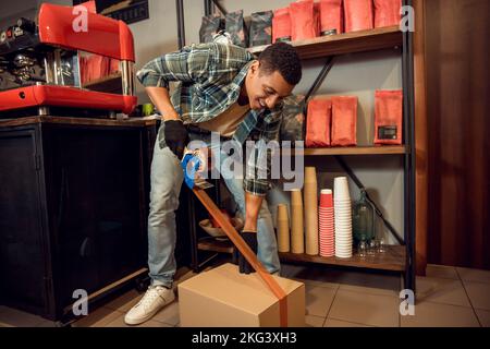 Joyful young cafe worker taping a closed carton Stock Photo