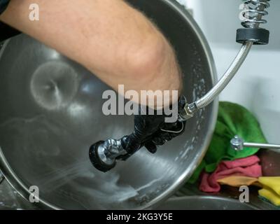 person cleaning a big stainless bowl in sink in industrial kitchen Stock Photo