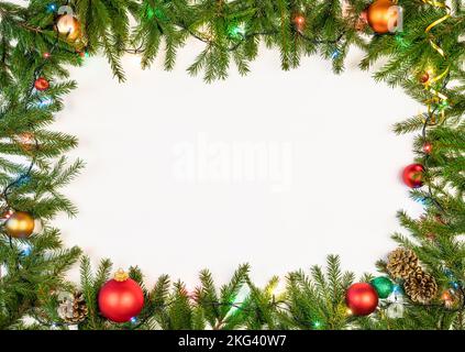 Christmas frame made of fir branches baubles cones and Christmas multicolored electric lights on white background Stock Photo