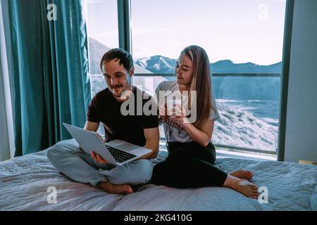 Couple at home sitting on the bad with laptop Stock Photo