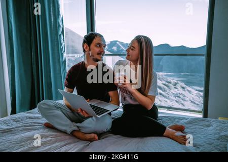 Couple at home sitting on the bad with laptop Stock Photo