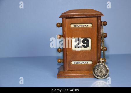 Antique desk calendar showing date of next leap year day 02.29.2024 with gold pocket watch lent against it and the chain draped over the date adjustme Stock Photo