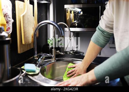 A woman washes dirty dishes in the kitchen sink Stock Photo
