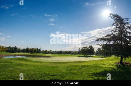 Panoramic view of grassy golf course with pond and trees located against cloudy blue sky on sunny summer day Stock Photo