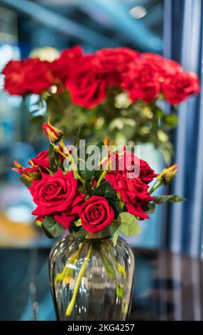 Bunch of fresh roses with red petals placed in glass vase on blurred background Stock Photo