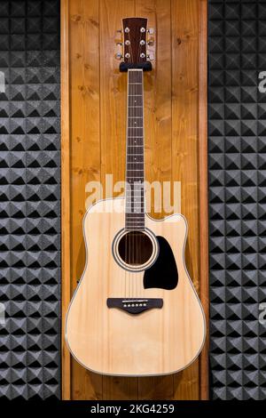 Wooden classic guitar with black figure on sounding board placed on wall of modern recording studio Stock Photo