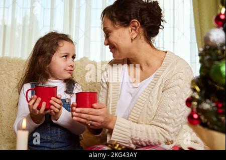 Multi-ethnic family of a loving mother and lovely daughter, with mugs of hot chocolate, enjoying happy moments together Stock Photo