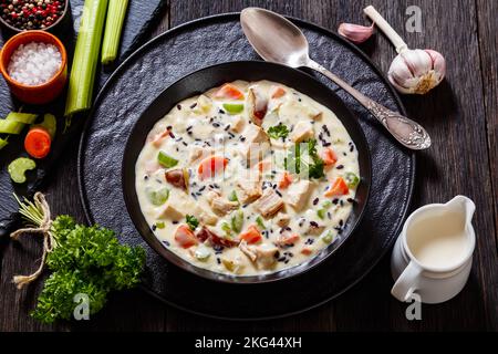 Turkey Wild Rice Soup with red potatoes. carrot, celery, spices and herbs in black bowl on dark wooden table with ingredients Stock Photo