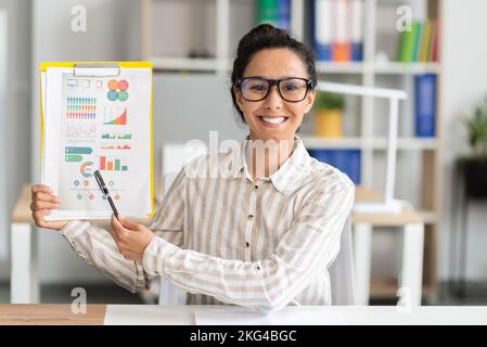Online meeting concept. Happy female manager having video call, showing diagrams to camera, sitting in office Stock Photo