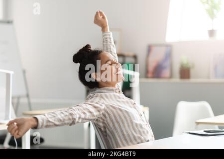 Relax at work. Happy young female manager sitting in office, stretching her back and arms, feeling pleased and satisfied Stock Photo