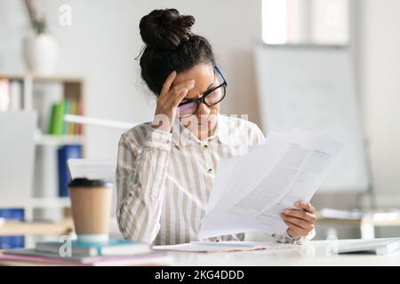 Paperwork concept. Tired female manager reading paper or financial document, sitting at desk in office Stock Photo