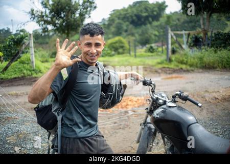 Filandia, Quindio, Colombia - June 5 2022: Young Colombian Man Waving at the Camara while Holding his Helmet and Motorcycle Stock Photo