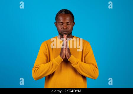 African american man praying with closed eyes on blue Stock Photo