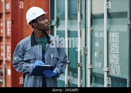 Waist up portrait of young black man wearing hardhat while working at shipping dock and holding clipboard Stock Photo