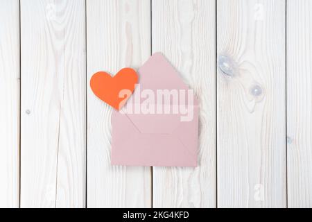 Pink opened envelope on white wooden background. Red cardboard heart is taken out of Valentine envelope. Copy space. Love, valentine, confession of Stock Photo