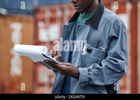 Cropped shot of young black man wearing hardhat and holding clipboard while working at shipping docks Stock Photo