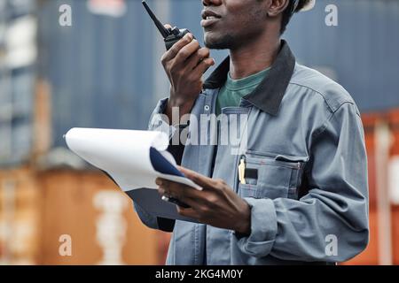 Cropped shot of young black man using walkie talkie while working at shipping docks with containers Stock Photo