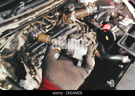 A mechanic hand holds an ignition coil for a spark plug in an automobile engine,isolated object on blurred background. Stock Photo