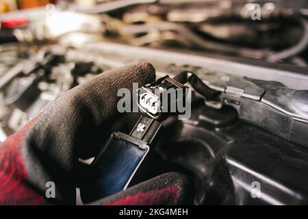The auto mechanic is unplugging the ignition coil of the car engine in the engine compartment. Stock Photo