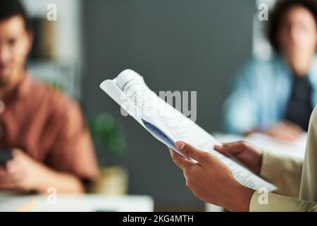 Focus on hands of young African American female speaker holding document while making report in front of audience at seminar Stock Photo