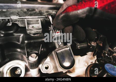 The auto mechanic is unplugging the ignition coil of the car engine in the engine compartment. Stock Photo