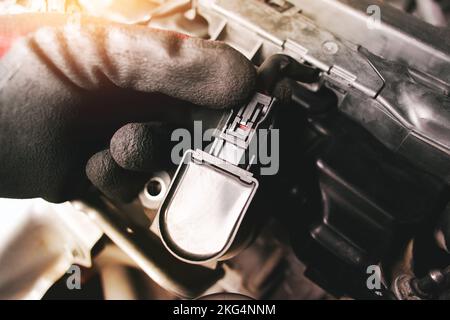 The auto mechanic is unplugging the ignition coil of the car engine in the engine compartment. Stock Photo