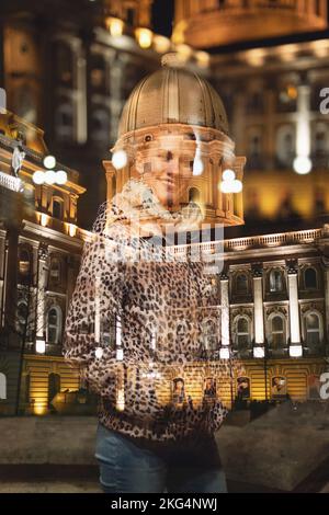 Happy young redhead hungarian urban woman in leopard pattern coat at winter toothy smile outdoor at night, Buda Castle, Budapest, Hungary. Double expo Stock Photo