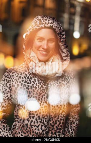 Young cheerful urban woman in leopard pattern coat toothy smile with bokeh at winter, hood on, double exposure Stock Photo