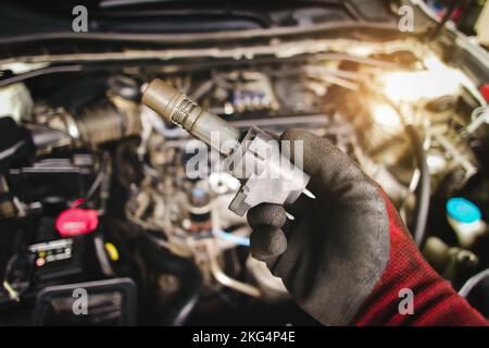 A mechanic hand holds an ignition coil for a spark plug in an automobile engine,  isolated object on blurred background Stock Photo