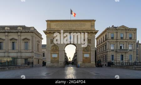 Early summer morning cityscape of ancient Arc de Triomphe or triumphal arch monument with French flag, historic landmark of Montpellier, France Stock Photo