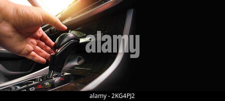 The driver hand is holding the gear lever to shift the automatic gear position in the car, horizontal banner copy space on black background Stock Photo