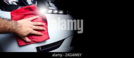 The owner hand is cleaning the front bumper with a cloth, panoramic banner with copy space on black background Stock Photo