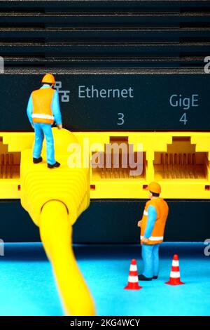 Conceptual image of miniature figure workmen investigating a fault on a broadband network cable Stock Photo