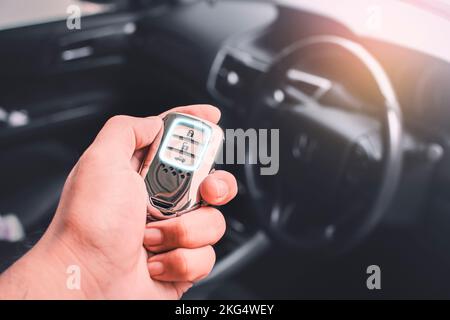 A automotive smart keyless entry held by the owner of the vehicle with a blurred background inside the vehicle and sunlight Stock Photo