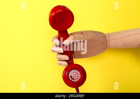 Wooden hand holding a red old fashioned retro telephone handset Stock Photo