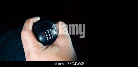 The driver hand is shifting the gears of a 6-speed manual transmission, panoramic banner with copy space on black background Stock Photo