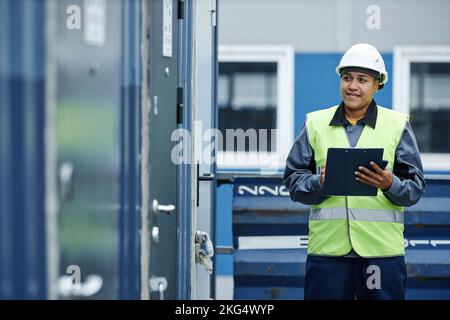 Graphic portrait of smiling female worker wearing hardhat while checking containers at shipping docks, copy space Stock Photo