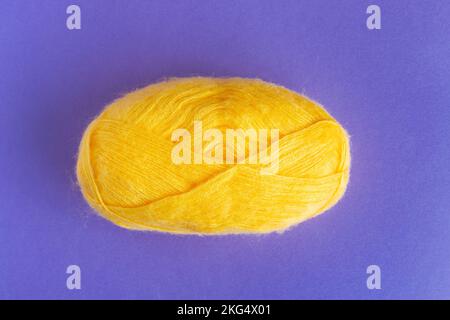 Yellow woolen roll of Yarn for knitting on purple, lilac background.  Stock Photo