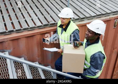 High angle portrait of two workers carrying boxes up stairs at shipping docks Stock Photo