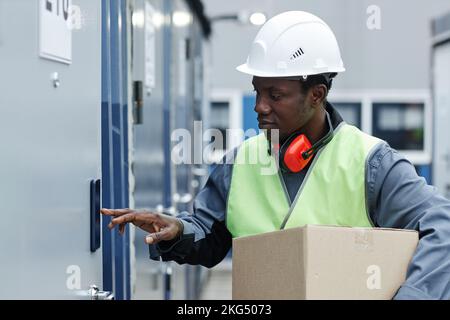 Side view portrait of black young man wearing hardhat while entering code on storage unit Stock Photo